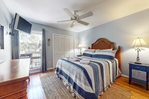 A bedroom with a bed, a ceiling fan, a TV mounted on the wall, a bedside table with a lamp, and a view of the outside through a window. - Beautiful Villa with screened in patio with perfect location (Edisto Beach)