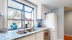 Eine Küche mit Fenster, Spüle, weißen Schränken und einem weißen Kühlschrank.