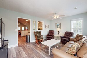 A living room with a sofa, chairs, a coffee table, and a ceiling fan. - Peaceful home close to the beach with EV Charger, screened-in porch, large yard (Edisto Beach)