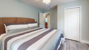 Ein Schlafzimmer mit Bett, Deckenventilator, einer Tür und einem zur anderen Kammer führenden Gang.