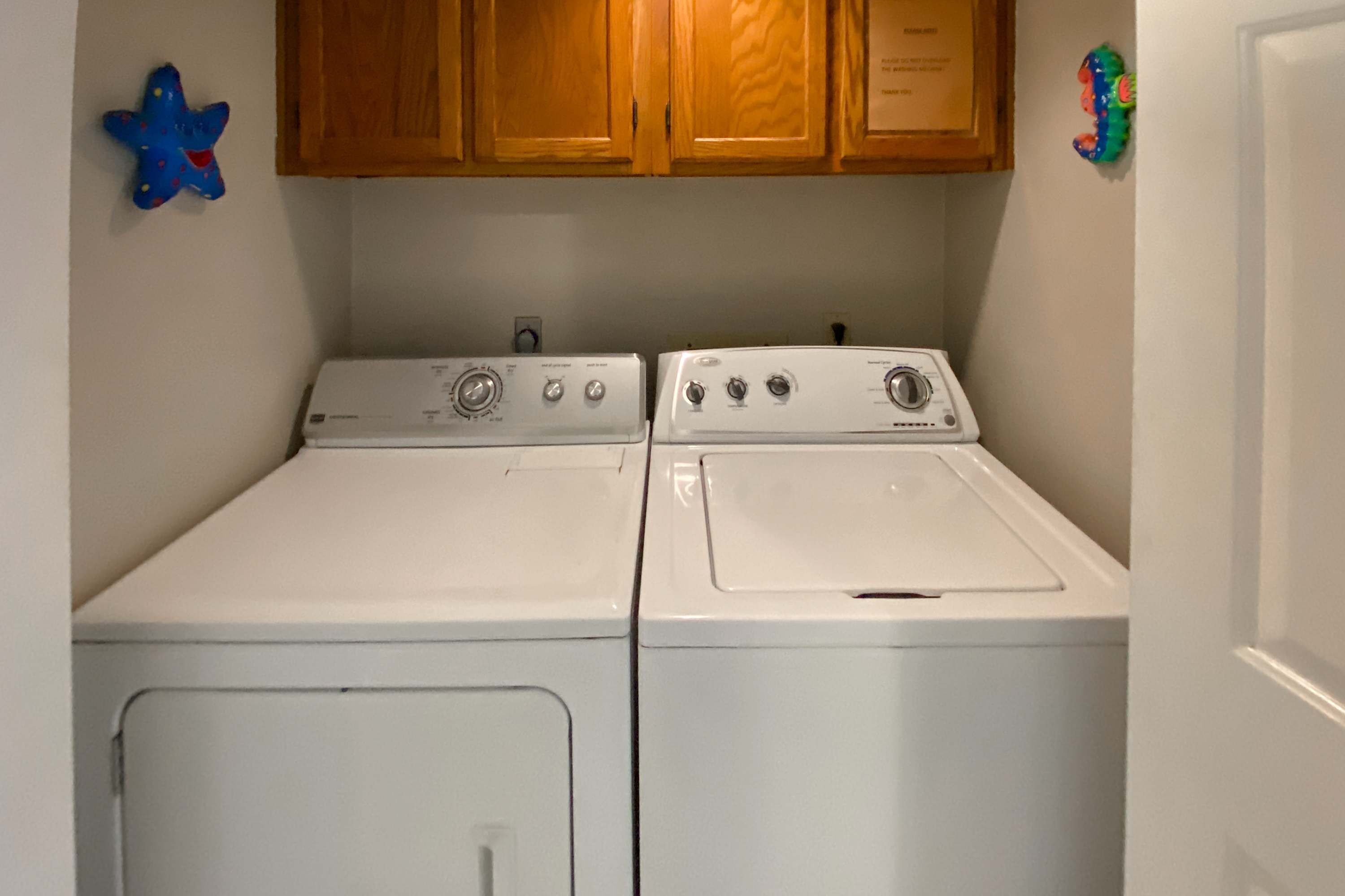 Een wasserette met twee witte wasmachines en drogers, houten kasten erboven, en een blauwe ster-vormige decoratie aan de linker muur.