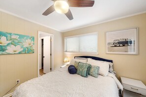 Une chambre à coucher avec un lit, un ventilateur de plafond, une fenêtre avec des stores et une porte.