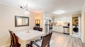 A dining area with a table, chairs, a chandelier, and a kitchen with appliances. - The Hedges D1 Condo in Hilton Head with pool & tennis, walk to the beach (Hilton Head)