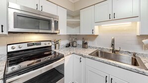 A kitchen with white cabinets, a stainless steel microwave, an oven, a sink, and a countertop with various utensils. - The Hedges D1 Condo in Hilton Head with pool & tennis, walk to the beach (Hilton Head)