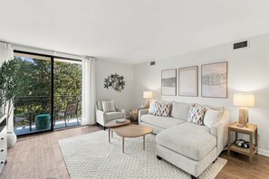 Un salon moderne comprenant un canapé, des fauteuils, une table basse et un balcon offrant une vue sur la verdure.
