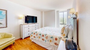 A bedroom with a bed, a television, a dresser, a chair, and a window.