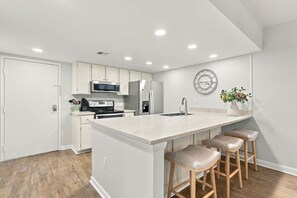 Une cuisine moderne avec des meubles blancs, des appareils en acier inoxydable, un grand îlot central doté de tabourets et une horloge murale.