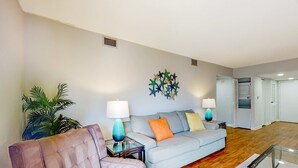 A living room with a sofa, armchairs, a coffee table, two lamps, a wall art piece, and a potted plant.
