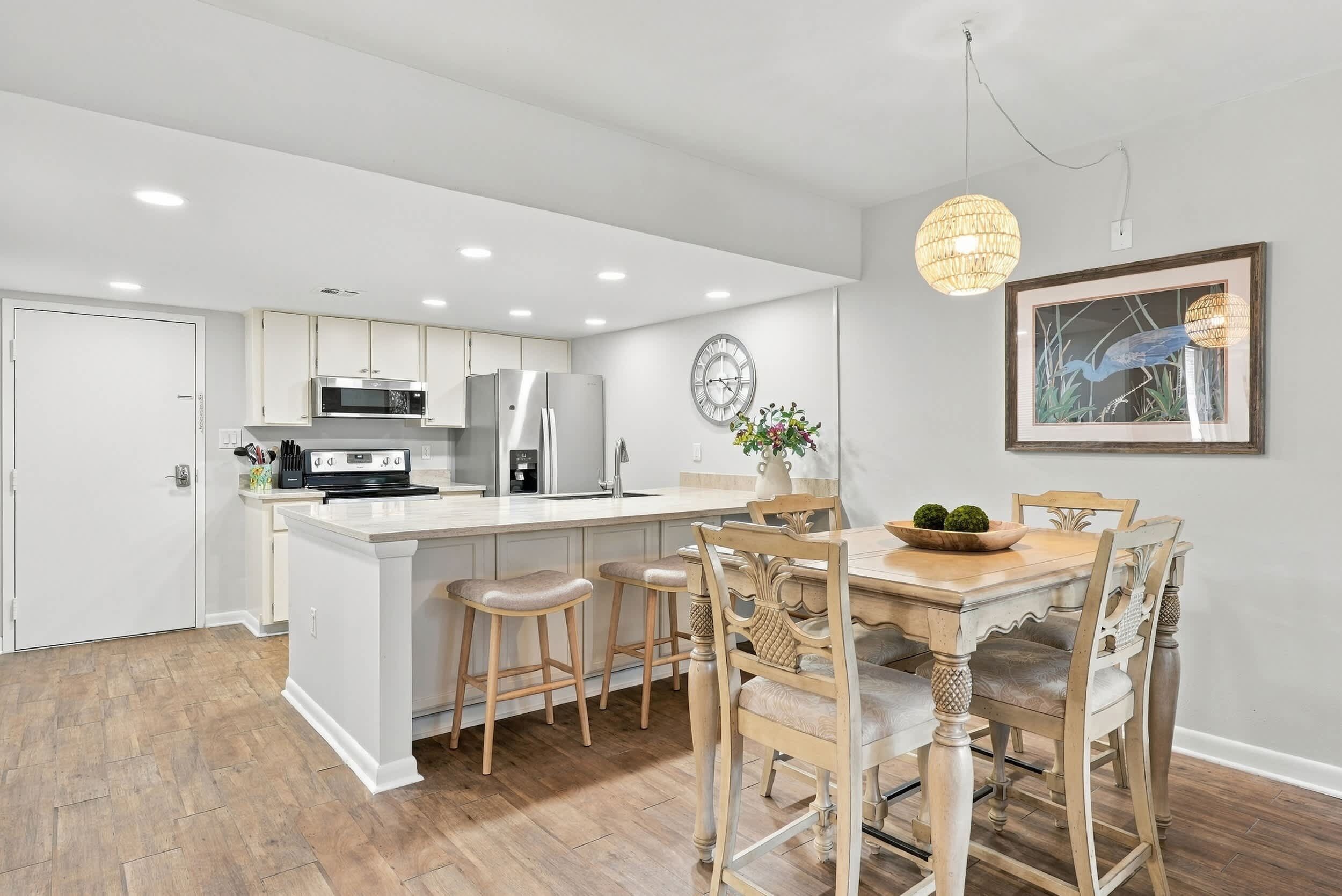 A modern kitchen with white cabinetry, stainless steel appliances, and a central island with bar stools.
