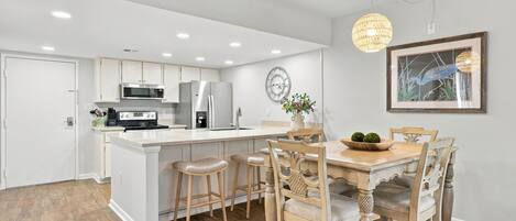 A modern kitchen with white cabinetry, stainless steel appliances, and a central island with bar stools.