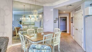Un espace repas avec une table en bois et des chaises blanches, un lustre et une cloison en verre.