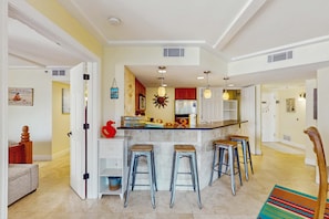 A kitchen with a central island, bar stools, and a dining area with a chair. - Stunningly remodeled 3rd floor villa with ocean views (Hilton Head)