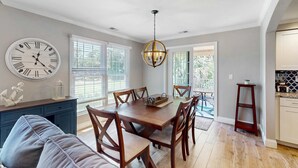 A dining area with a wooden table, chairs, a chandelier, and a clock on the wall. - Stunningly remodeled villa with shared pool and golf on-site (Hilton Head)