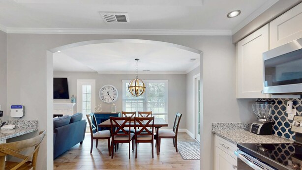 A modern kitchen with a dining area, wooden chairs, a chandelier, and a kitchen island. - Stunningly remodeled villa with shared pool and golf on-site (Hilton Head)