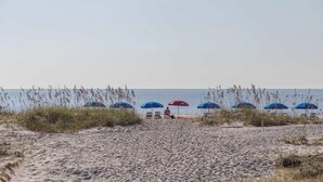 Ein Strand mit Sand, einer Person und mehreren Sonnenschirmen.