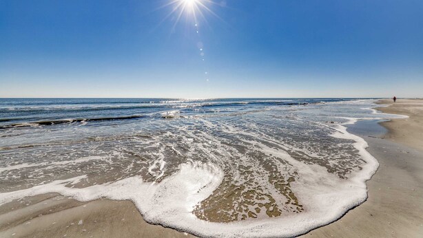 Una playa con olas, cielo despejado y sol brillante.
