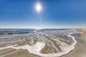 En strand med vågor, en klar himmel och en skinande sol.