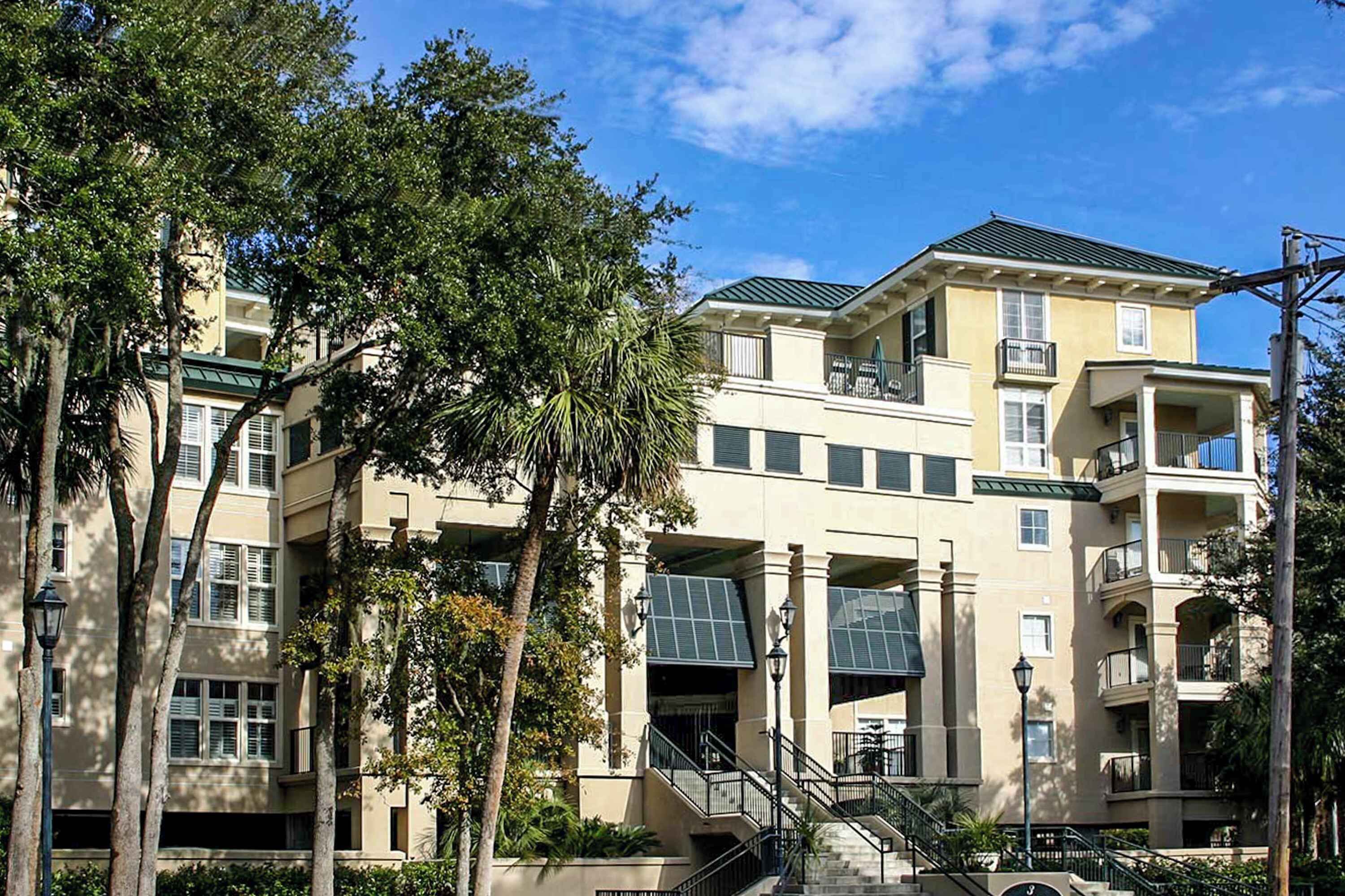 A multi-story building with balconies, a central staircase, and surrounding trees.