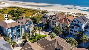 Zona residencial costera con propiedades frente al mar, incluyendo casas de varios pisos con balcones, una vista despejada de la playa y un sendero que conduce a ella.