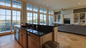 Una cocina amplia con ventanas grandes, una isla central y un sofá gris en una sala de estar.