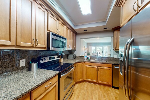 A modern kitchen with granite countertops, stainless steel appliances, wooden cabinets, and a skylight. - Oceanview and Pool view Condo- with beach access from boardwalk (Hilton Head)