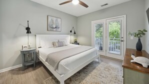 Ein Schlafzimmer mit Bett, Nachttisch, Deckenventilator, Fenster und Tür.