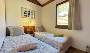 Un dormitorio con dos camas, una foto enmarco de Brittany, una ventana con persianas y una lámpara de noche.