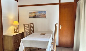 Una habitación con una cama, una mesita de noche con lámpara, un cuadro en la pared y una puerta de madera.