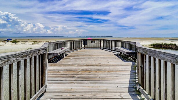 Una passerella di legno che conduce a una spiaggia sotto un cielo sereno.