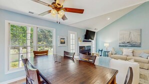 Un espace repas avec une table et des chaises en bois, un ventilateur de plafond et de grandes fenêtres.