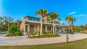 Een modern huis met twee verdiepingen, een overdekte patio, palmbomen en een verzorgd gazon.