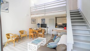 Un espacio habitable moderno con comedor, sofá, escalera y cocina visible a través de un vidrio.