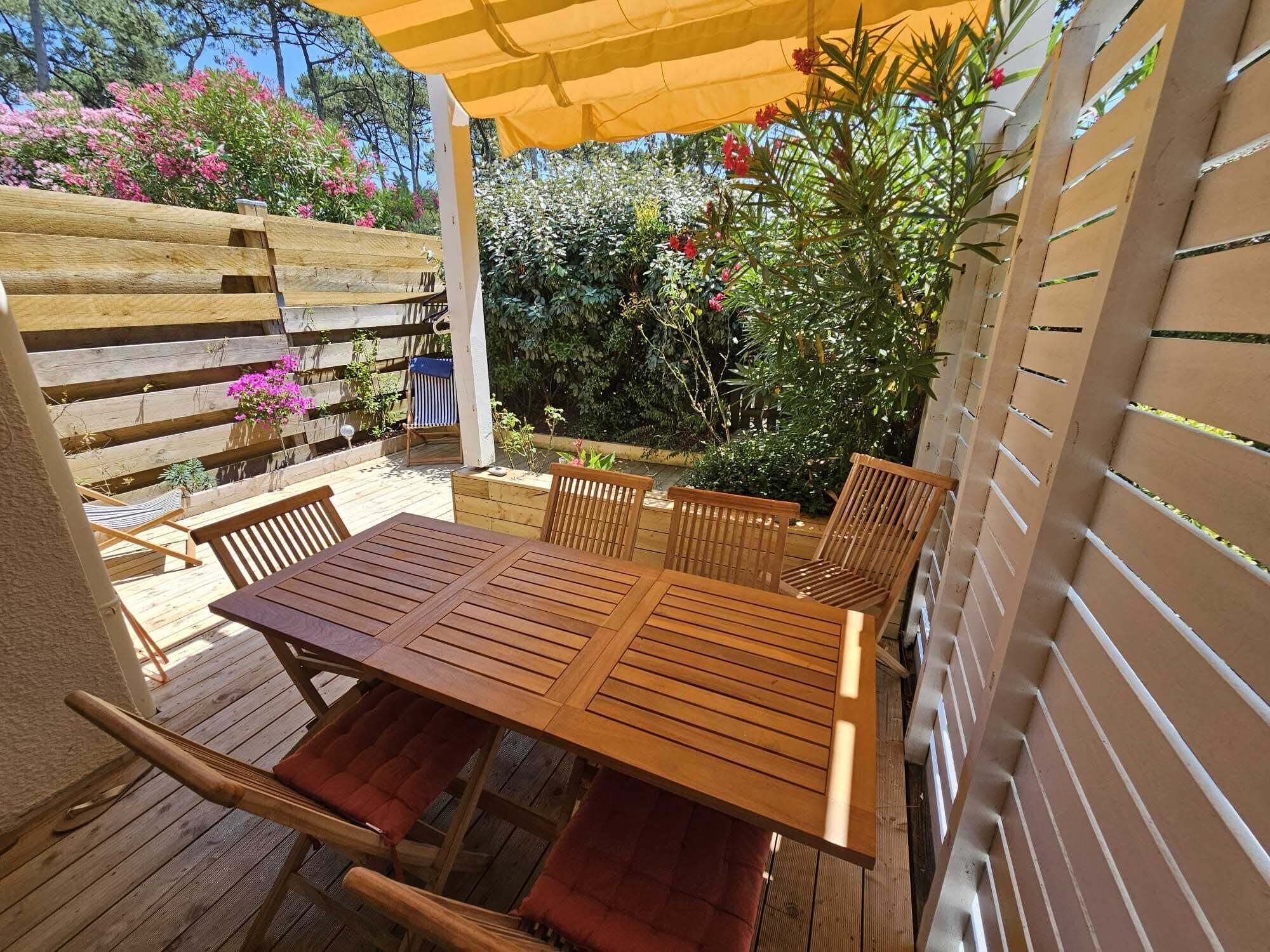 A wooden deck with a table and chairs, surrounded by a wooden fence and plants.