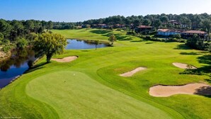Un campo de golf con búnkeres, un estanque y edificios residenciales al fondo.