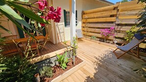 Una terraza de madera con una silla, una hamaca y un pequeño jardín con plantas y flores.