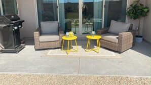 Eine Terrasse mit Korbmöbeln, einem Grill und einer Schiebetür.
