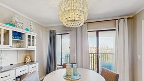 A modern room with a round table, a chandelier, a balcony with curtains, and a view of the city. - Beachfront condo w pool, tennis and pickleball, gym & balcony (Hilton Head)