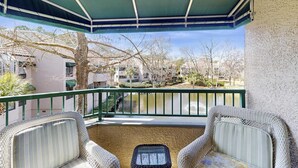 A balcony with two wicker chairs, a green awning, and a view of a water body and buildings. - Lagoon views, shared pool and easy access to Shelter Cove Towne Center (Hilton Head)