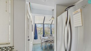 A kitchen with a refrigerator, a dining table with chairs, a window with curtains, and a ceiling fan. - Lagoon views, shared pool and easy access to Shelter Cove Towne Center (Hilton Head)