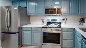 Una cocina con armarios azul claro, electrodomésticos de acero inoxidable y suelo de baldosas.