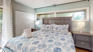 Un dormitorio con cama, mesitas de noche, una ventana y una puerta.