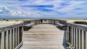 Une promenade en bois menant à une plage, avec un ciel dégagé.
