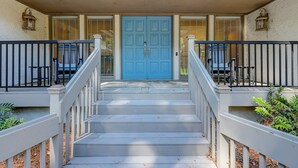 Eine Ansicht der Vorderseite eines Hauses mit einer blauen Tür, weißen Geländern und Stufen zum Eingang.