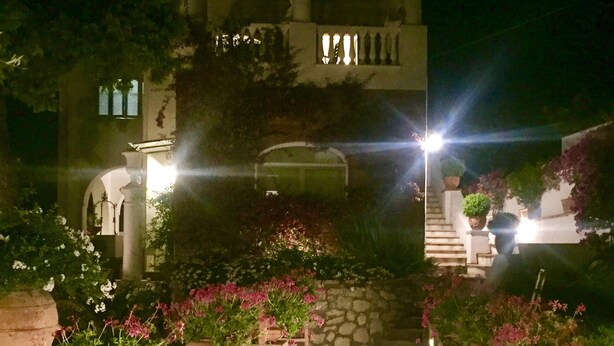 Une vue nocturne d’un chemin bordé de jardinières menant à un bâtiment doté d’un balcon.