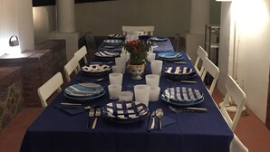 Une table à manger dressée avec de l’argenterie bleue et blanche, des chaises blanches et un arrangement floral central.