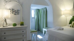 Une chambre à coucher comprenant un lit, une table de chevet, une commode, un miroir, une fenêtre avec des rideaux et un couloir menant à une autre pièce.