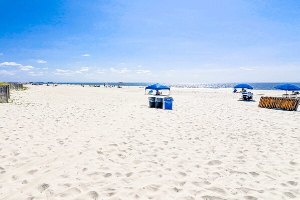A sandy beach with blue umbrellas and beach chairs. - Newly Renovated Coastal Condo with Ocean-View Balcony, Shared Pool & Easy Beach Access (Hilton Head)