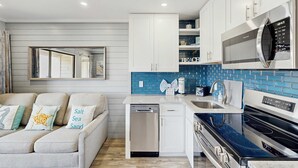Een moderne keuken met witte kasten, een blauwe achterwand, een ingebouwde magnetron en een vaatwasser.