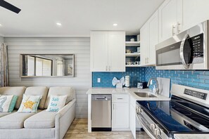 A modern kitchen with white cabinets, a blue backsplash, a built-in microwave, and a dishwasher. - Newly Renovated Coastal Condo with Ocean-View Balcony, Shared Pool & Easy Beach Access (Hilton Head)
