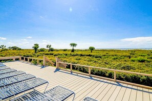 A wooden deck with lounge chairs and a view of a manicured landscape with trees and shrubs. - Newly Renovated Coastal Condo with Ocean-View Balcony, Shared Pool & Easy Beach Access (Hilton Head)